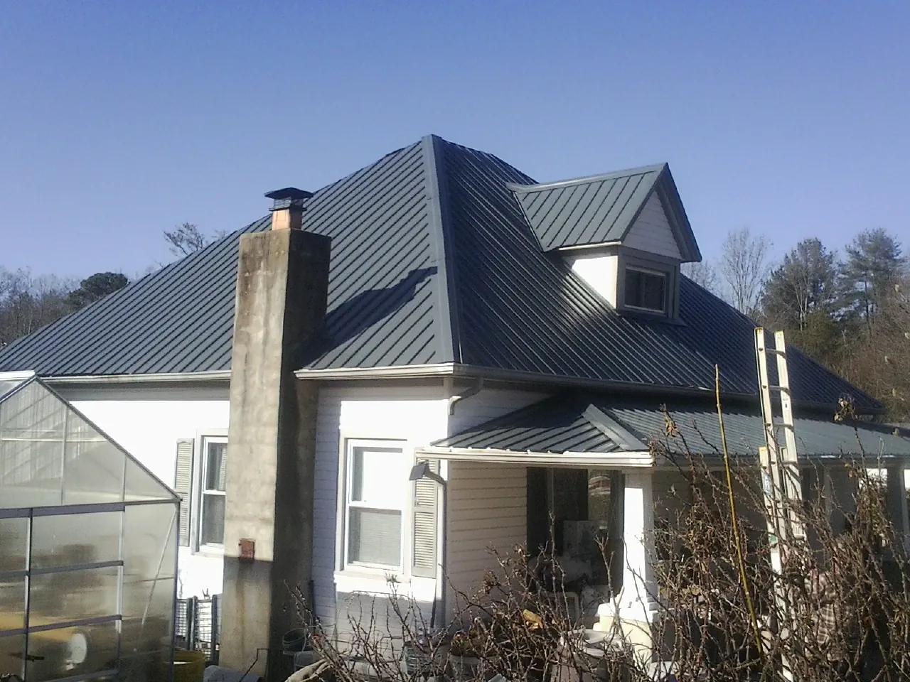 Dark blue standing seam metal roof on a white farmhouse with dormer — Slate & Tile Roof Repair by Roofing Brothers in Whitakers