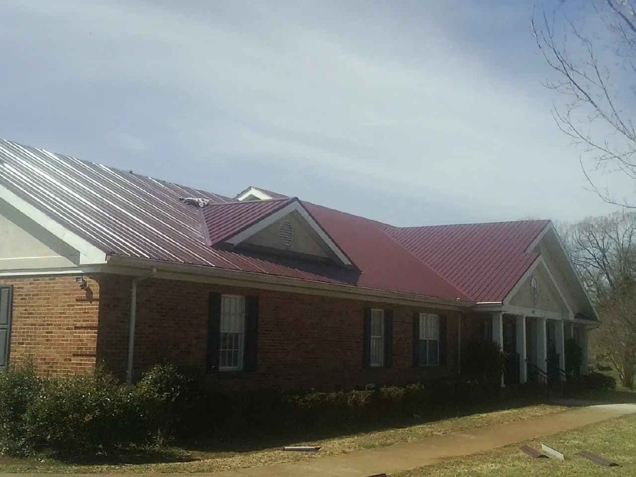 Red metal roof with gabled entries on a long brick building, from a Hail Damage Roof Repair job in Whitakers