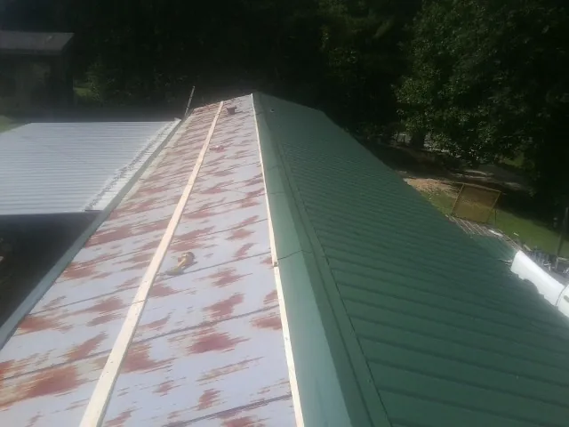 Old rusted panels beside newly installed green metal roofing — Wind Damage Roof Repair by Roofing Brothers in Whitakers
