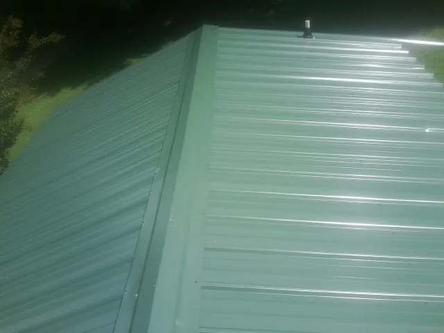 New green metal panels meeting at the ridge of a roof — Flat Roof Repair work by our crew in Whitakers