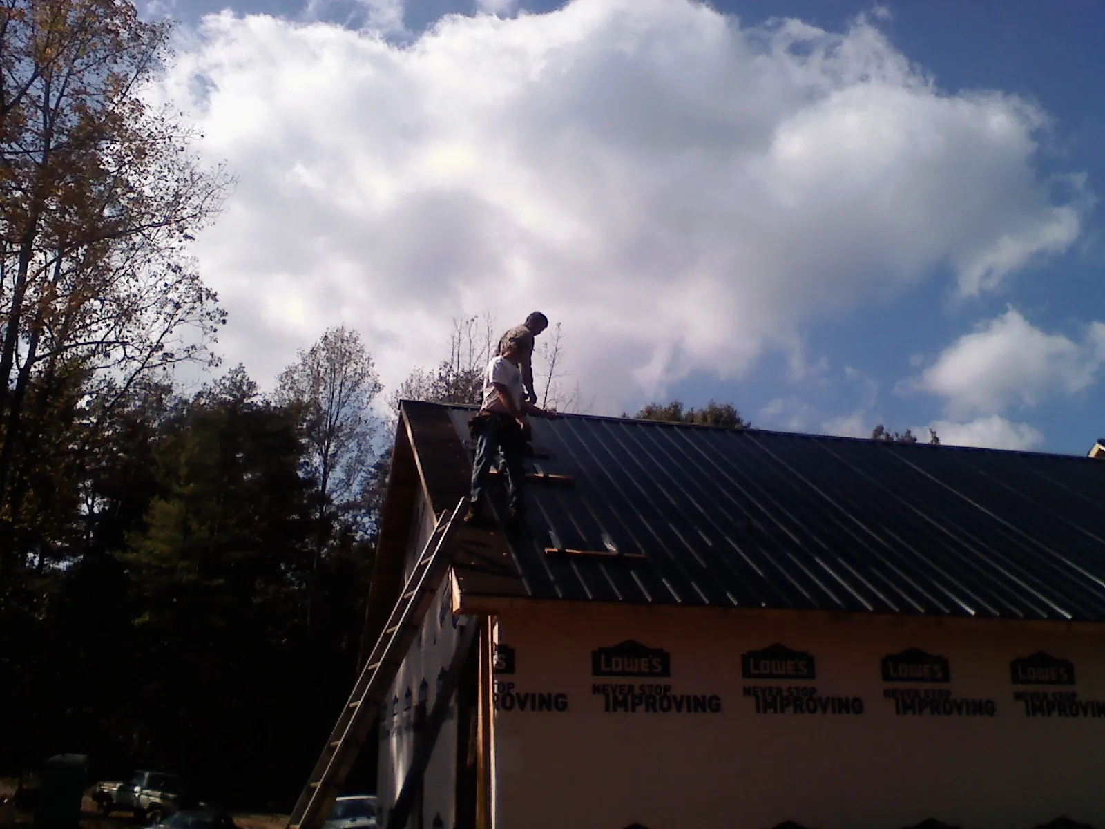 Roofer fastening dark metal panels high against a cloudy sky, from a Roof Inspection job in Whitakers
