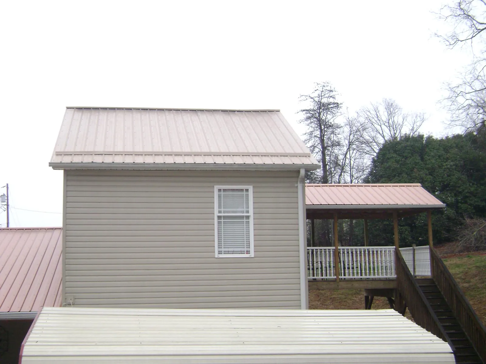 Tan metal roofs on a two story addition and attached porch, from a Roof Replacement job in Whitakers