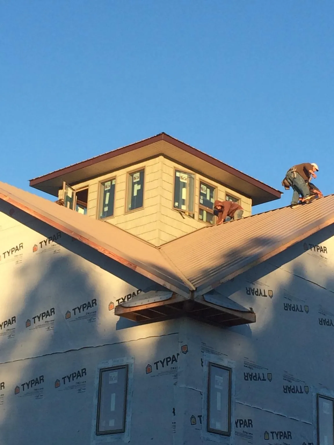 Roofers working around a rooftop cupola on a new metal roof at sunset — Roof Waterproofing in Whitakers by Roofing Brothers